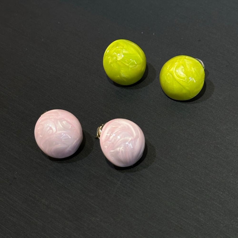 Two pairs of round earrings, one pink and one green, on a dark surface.