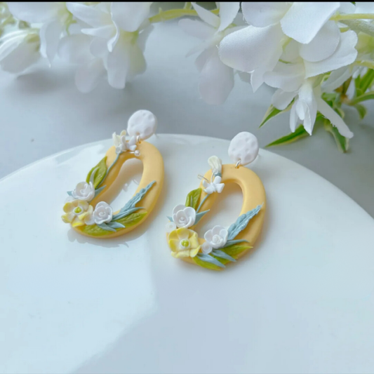 Yellow hoop clay earrings with floral details on a white surface with flowers in the background