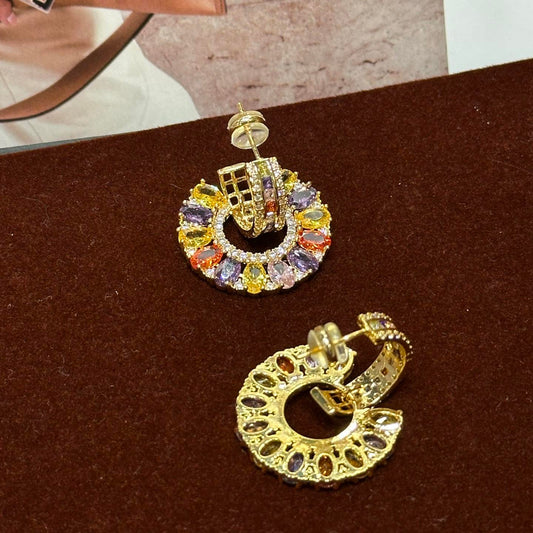 Gold hoop earrings with colorful gemstones on a brown surface