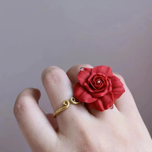 Red rose-shaped clay ring on a finger against a plain background
