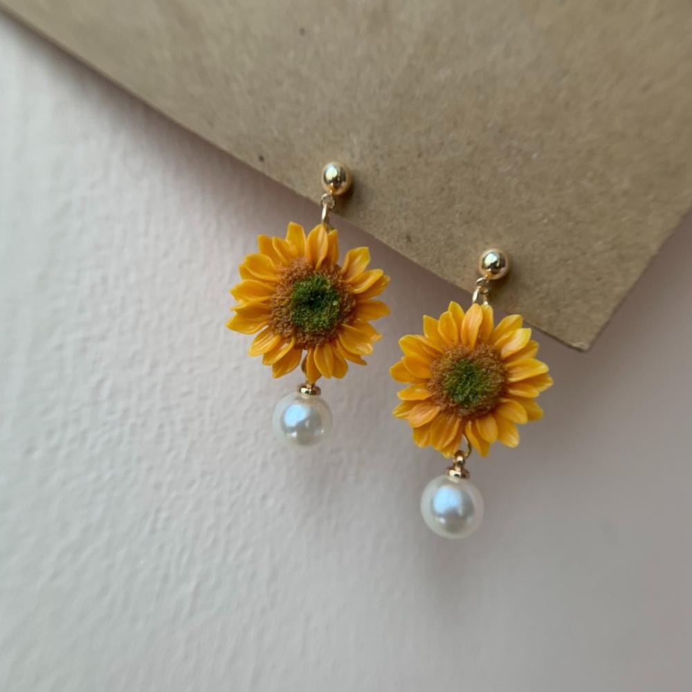 Sunflower earrings with pearl drops on a light background